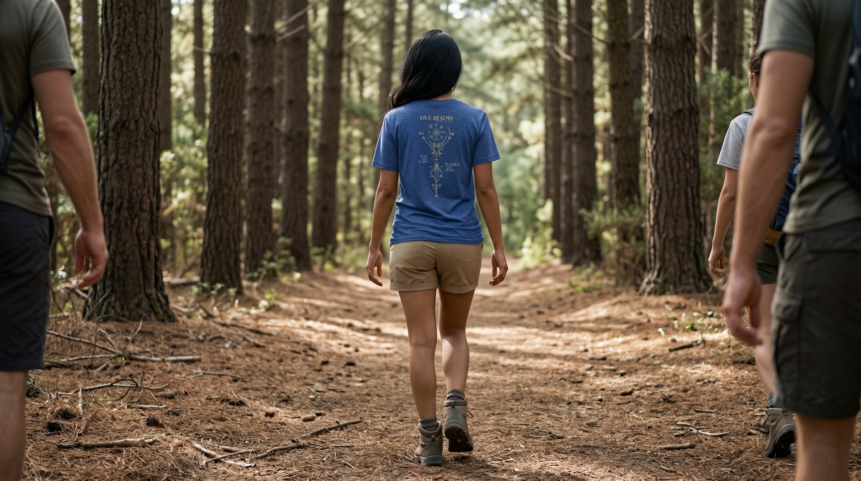 Woman with long black hair wearing a blue T-Shirt with a gold colored design on it walking on a forest path with others around