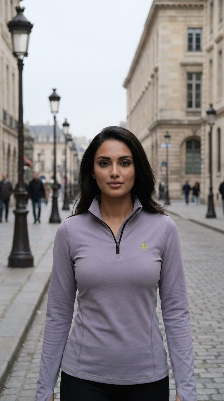 Woman wearing a light purple long-sleeve shirt with a logo on a city street.